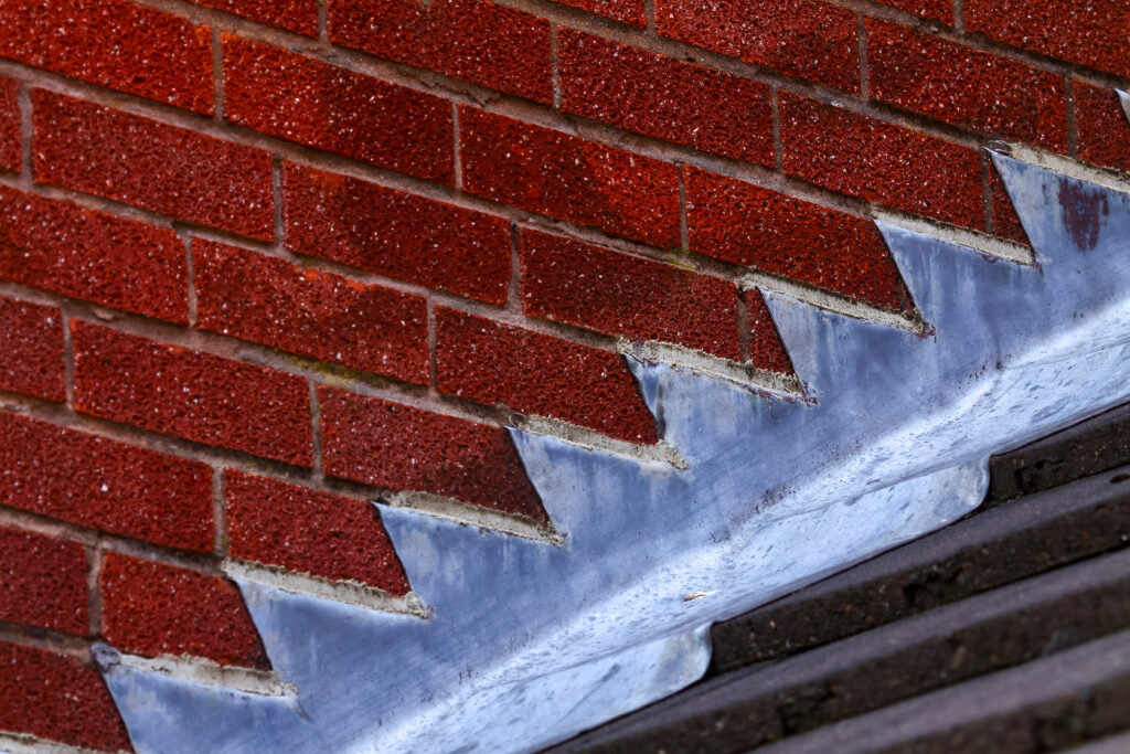 roof flashing repair Brown asphalt shingled roof valley leaking problem area with a ventilation cap. A close-up of asphalt shingles installed on a roof valley with a waterproof flashing. Asphalt shingles roofing.